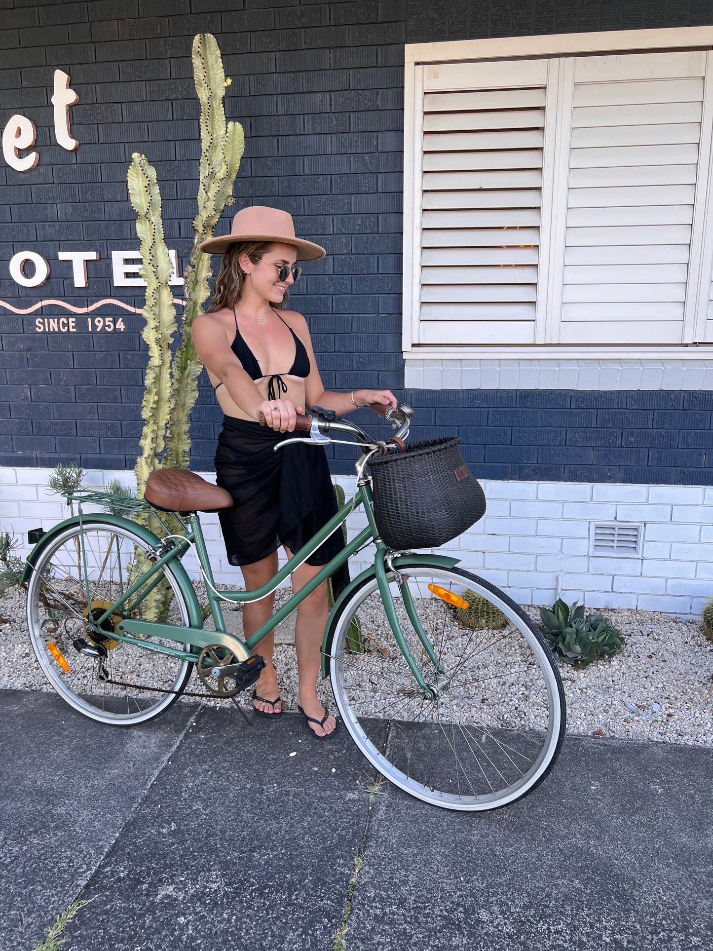 Berach girl with her green cruiser bike with black bicycle basket outside a trendy hotel